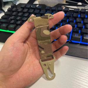 Hand holding a camouflage-patterned keychain with a hook in front of a keyboard